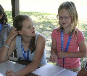 Bailey Boyer, 7, of Lake Orion, works with activity leader Abby Martin, 14, of Oxford, to describe in her journal how she felt during the activity where she was blindfolded and had to complete various tasks. Photo by Cathy Kimmel-Srock.